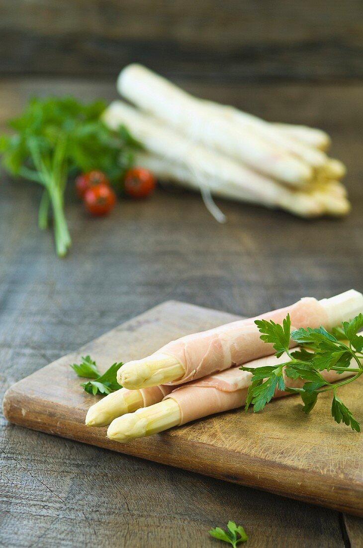 Raw white asparagus wrapped in ham on a chopping board