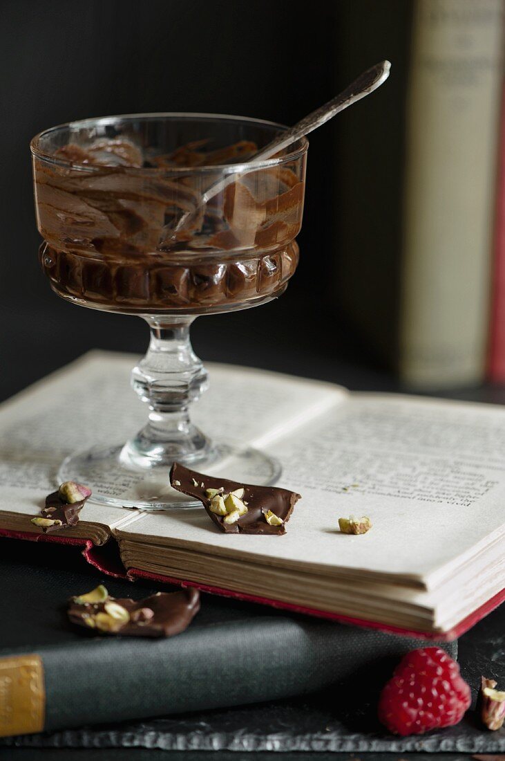 Dessertglas mit Resten von Mousse au Chocolate auf aufgeschlagenem Buch stehend