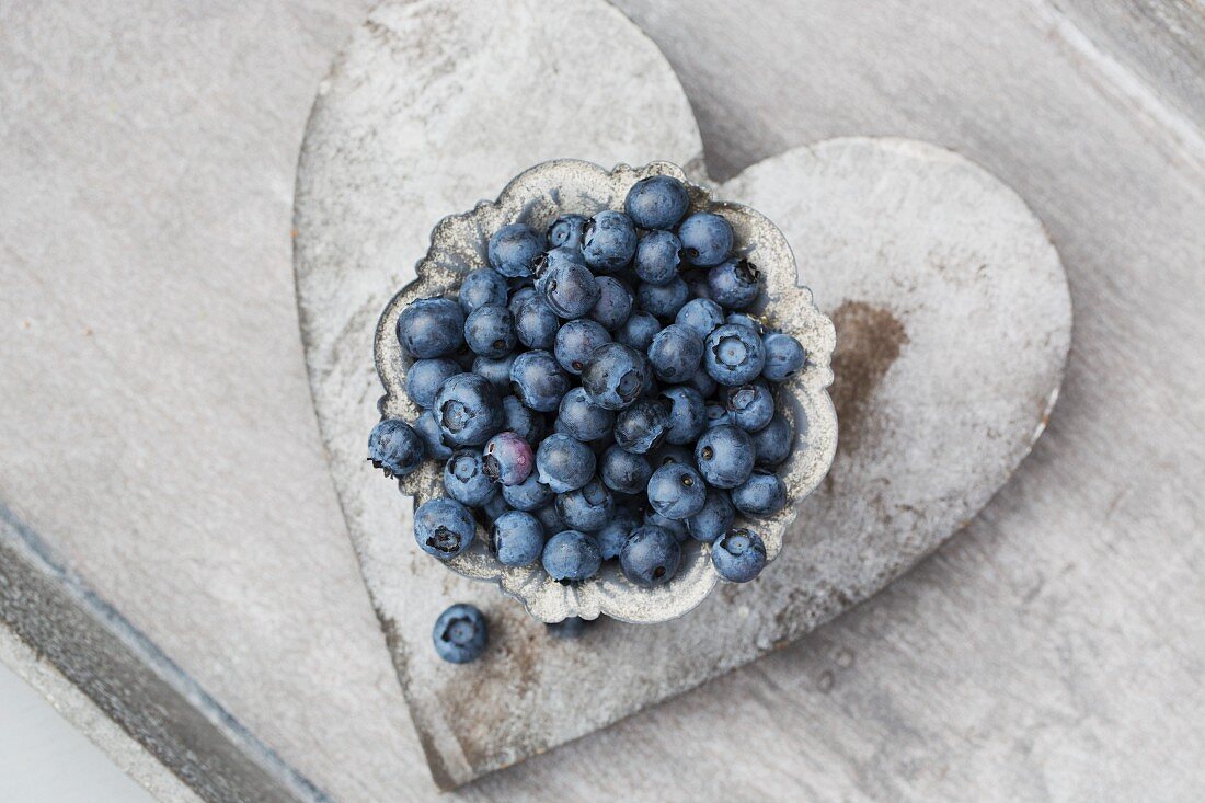 Fresh blueberries in a grey metal bowl on a heart-shaped coaster