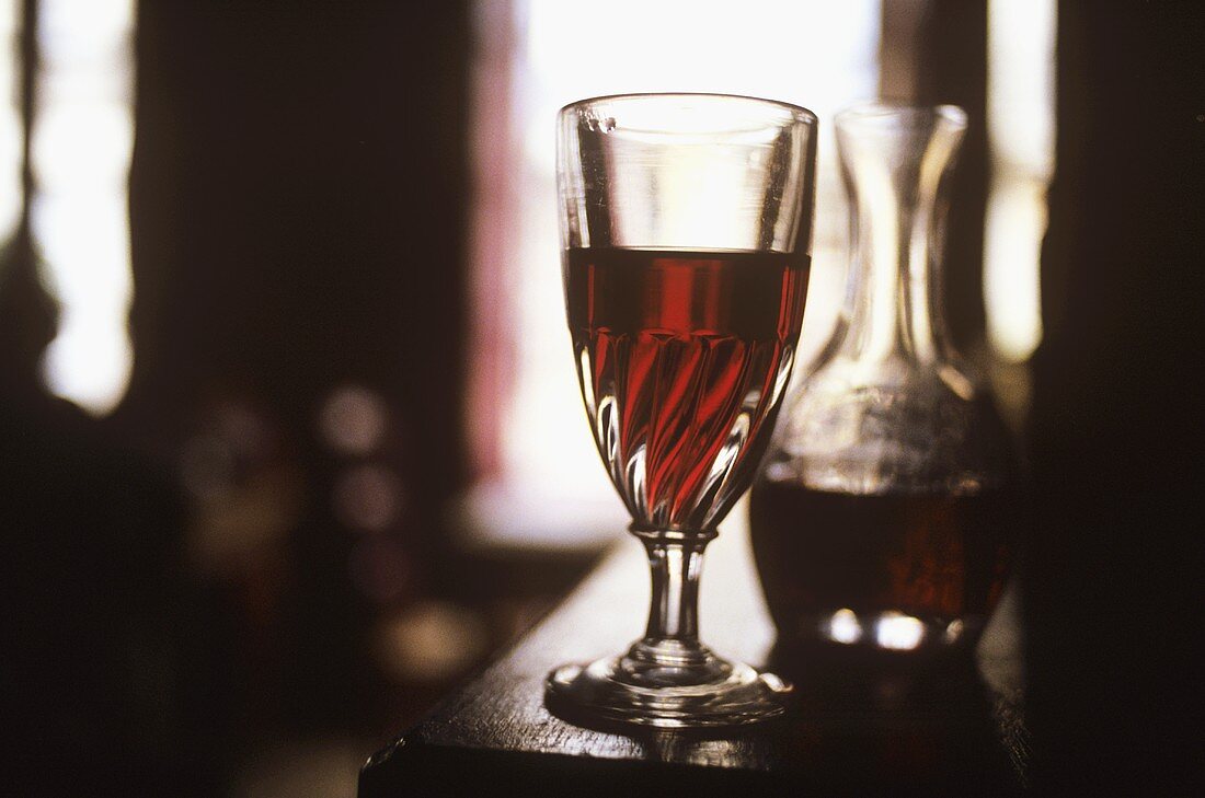 Still life with a glass of red wine in front of a carafe