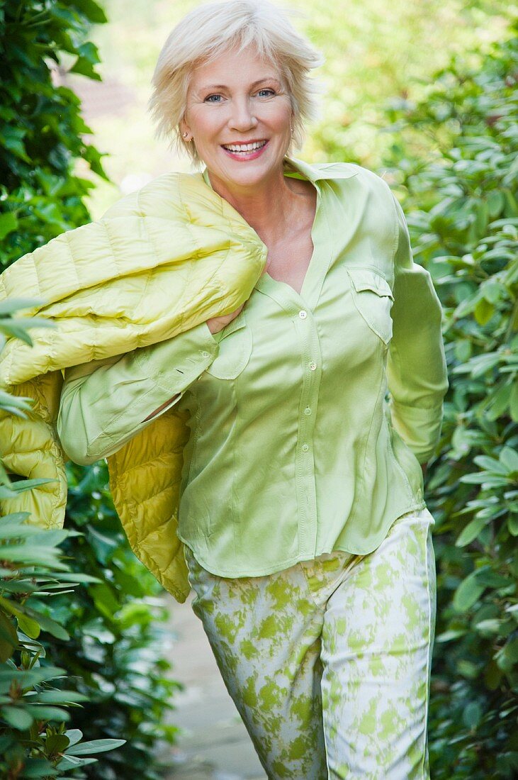 An older woman wearing a light green blouse and green-and-white trousers in a garden