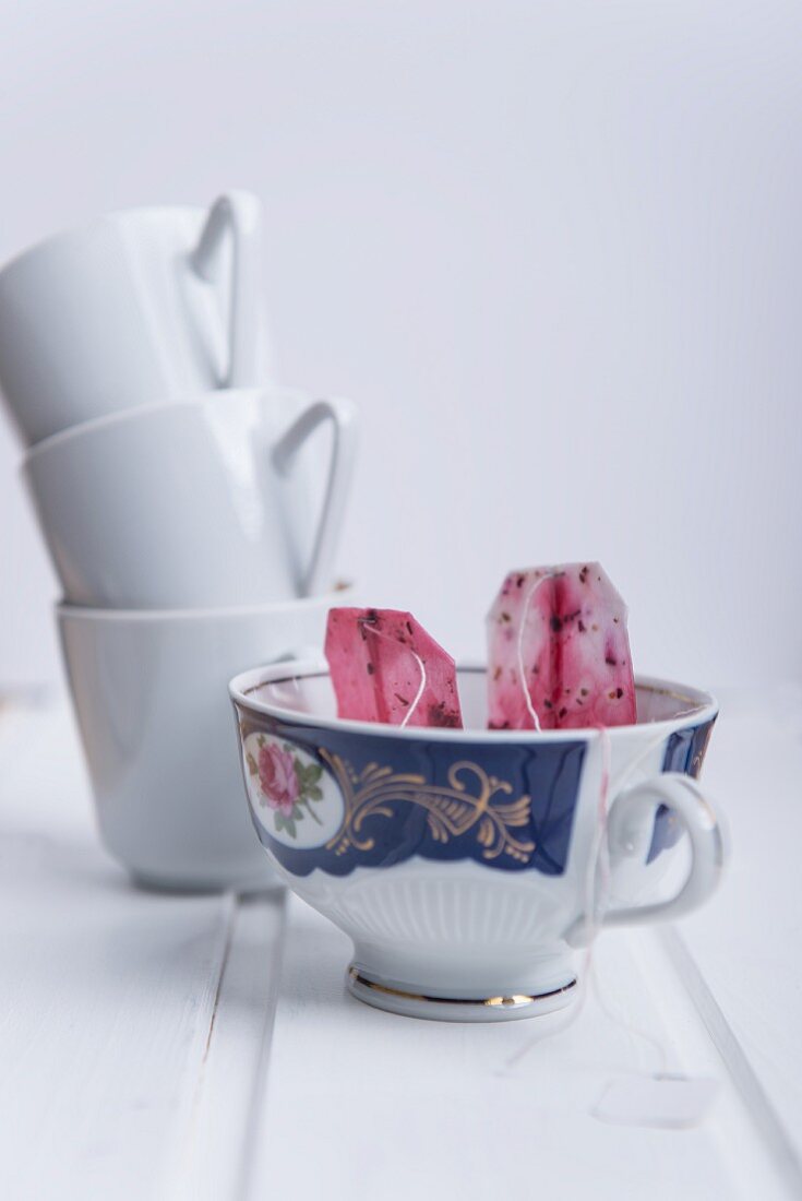 Used fruit tea bags in a porcelain cup with a stack of mugs in the background