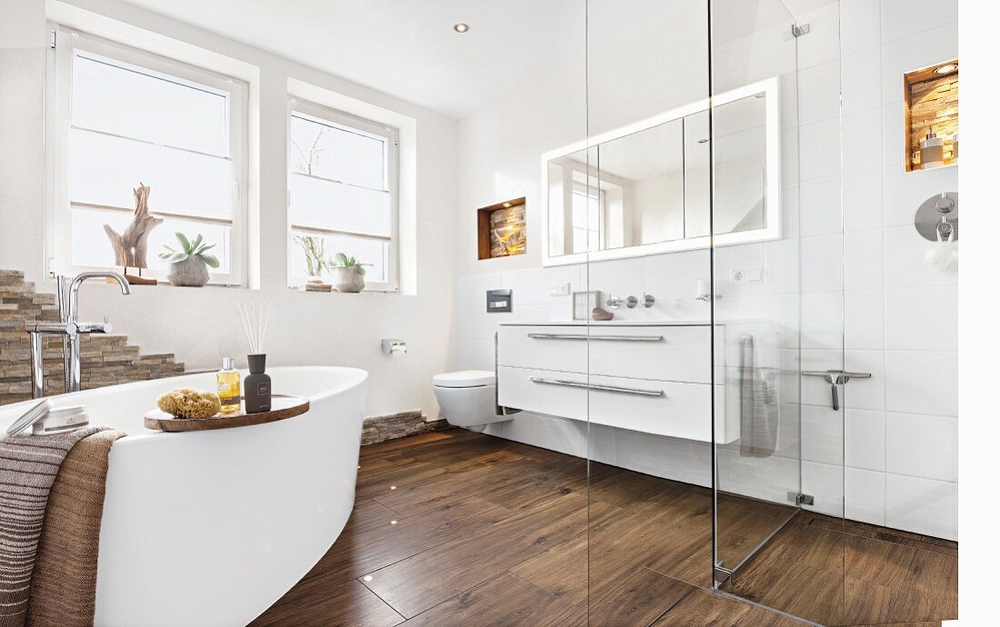 A modern bathroom with a warm, cosy atmosphere thanks to dark, wooden-style floor tiles and a free-standing oval bathtub