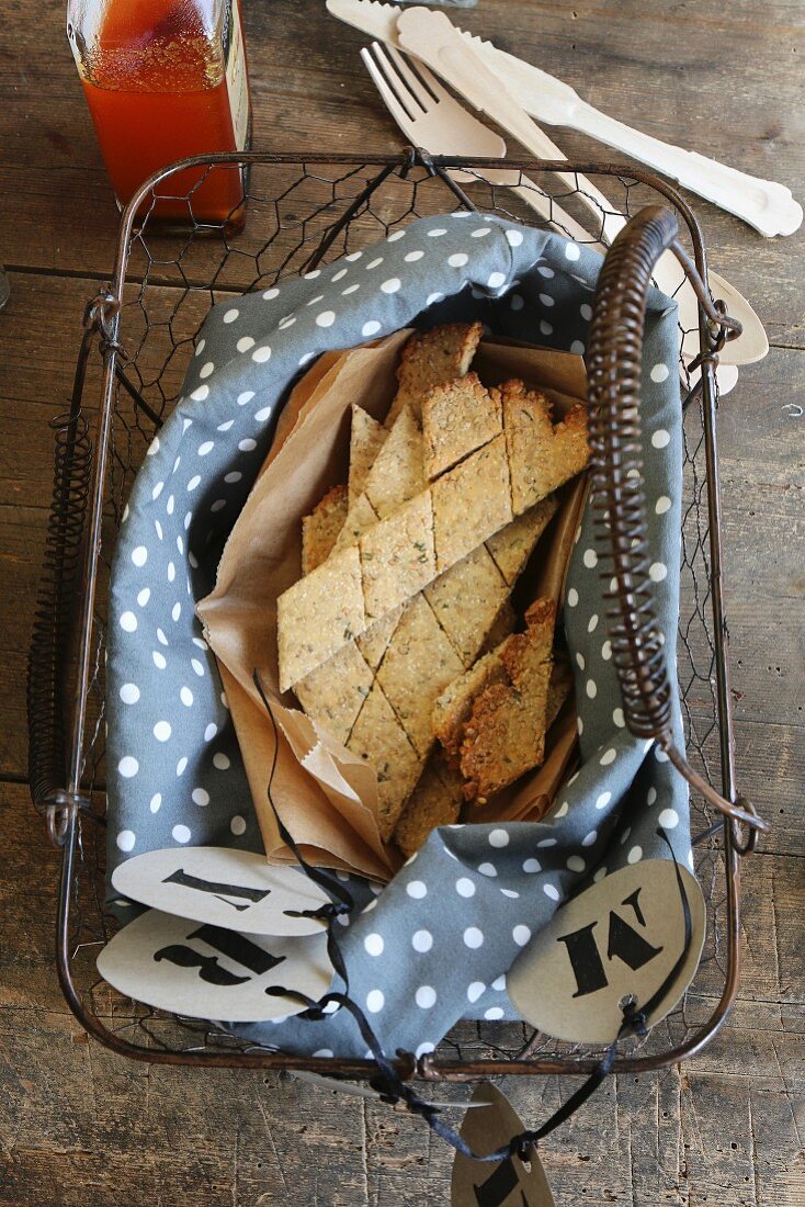 Gluten-free crackers with rosemary and sesame seeds on a blue and white polka dot cloth in a vintage wire basket