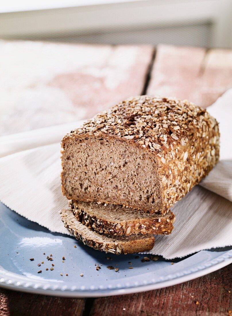 A loaf of wholemeal rye bread with seeds on a plate with two slices cut off