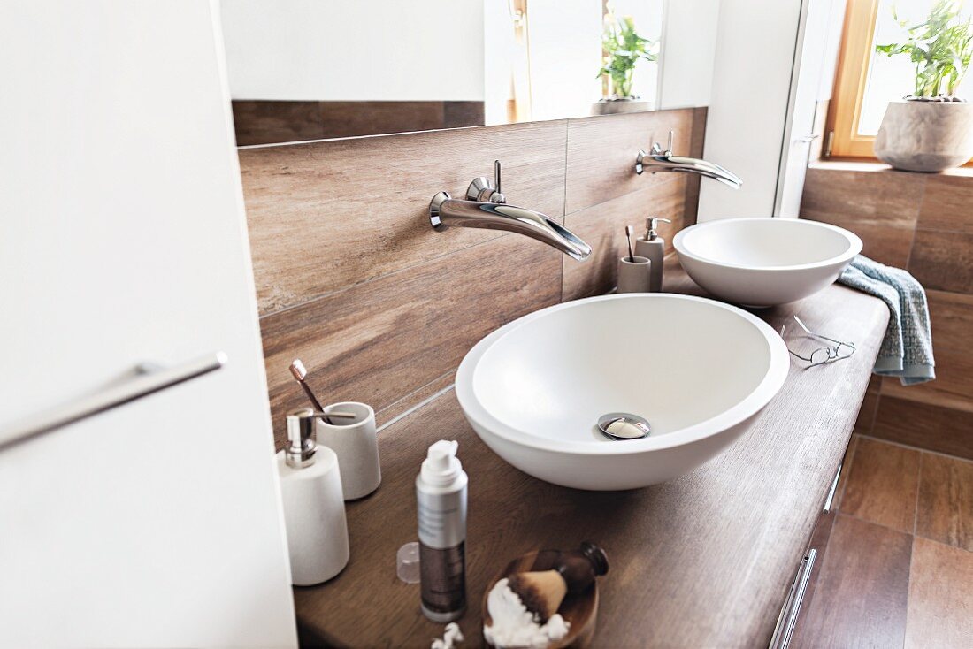 Two countertop basins on solid oak washstand, taps mounted on wall with wood-effect tiles