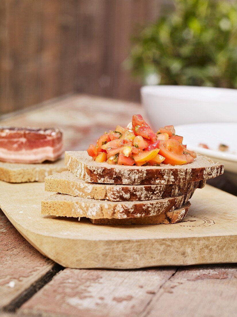 Slices of moist rye bread stacked on a chopping board and topped with tomato salad