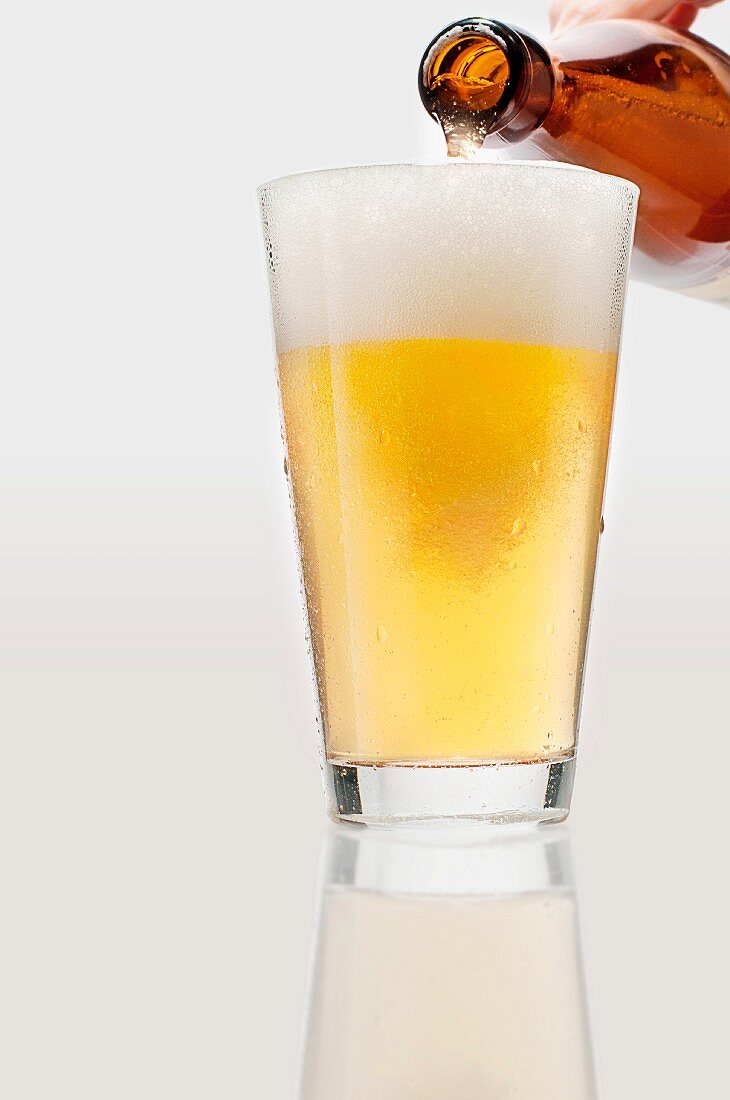 Helles Bier wird aus Flasche in Bierglas eingegossen