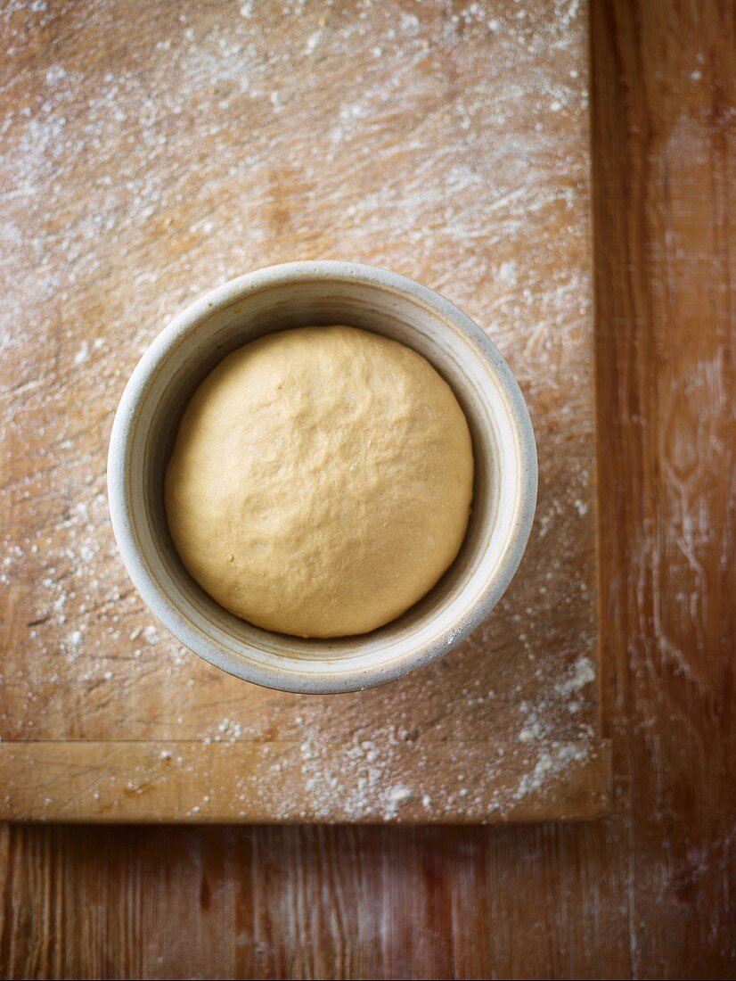 Bread dough in a porcelain dish on a floured wooden board (seen from above)