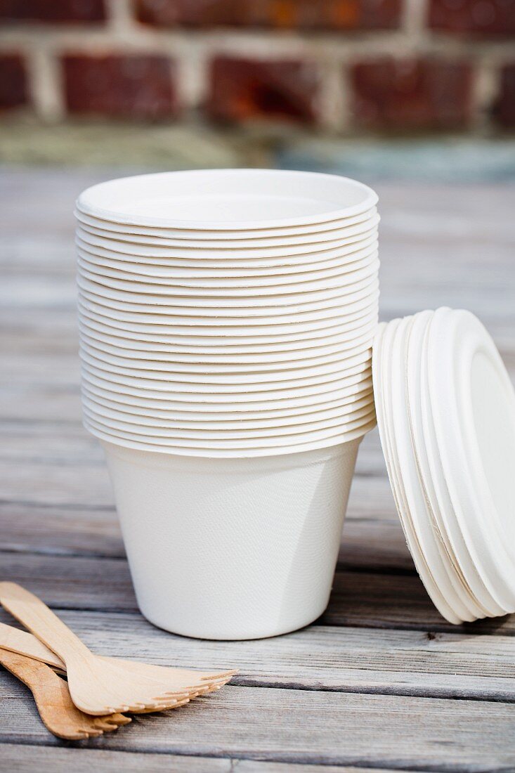 A stack of take-away cups and wooden forks on a table outside