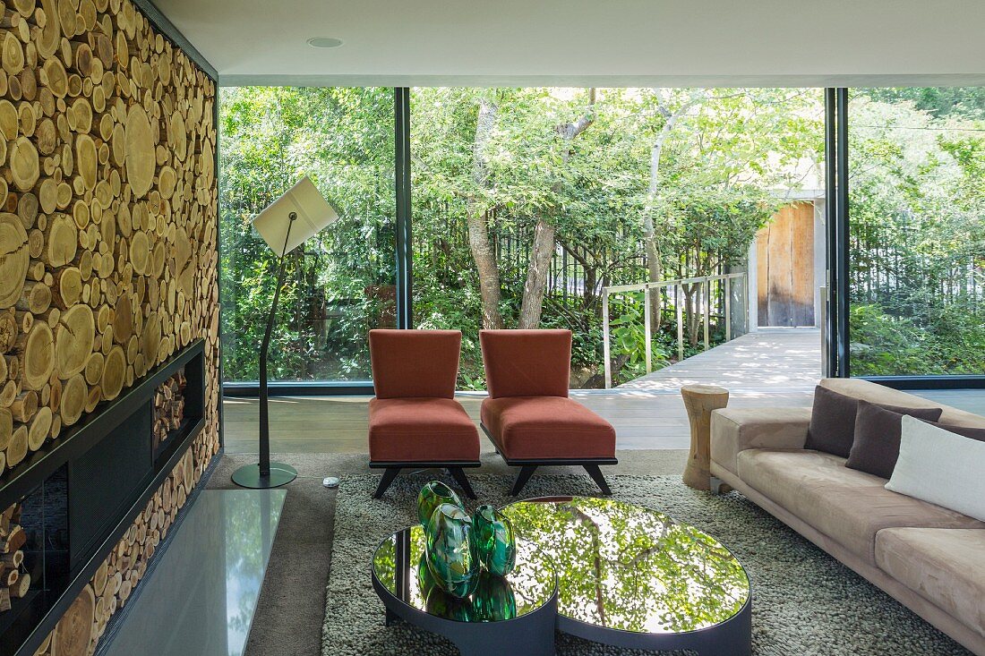 Designer sofa, chaise armchairs and mirrored coffee table in front of fireplace in wall decorated with slices of tree trunk