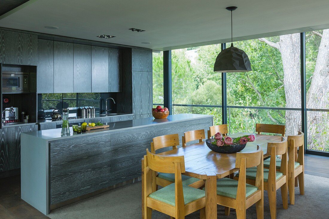 Oak dining set in front of kitchen with wooden cabinets in modern interior with glass wall