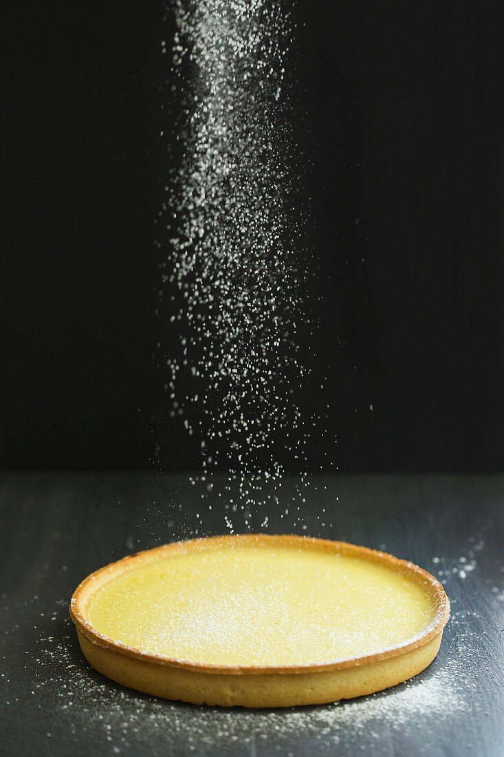 Lemon tart being dusted with icing sugar