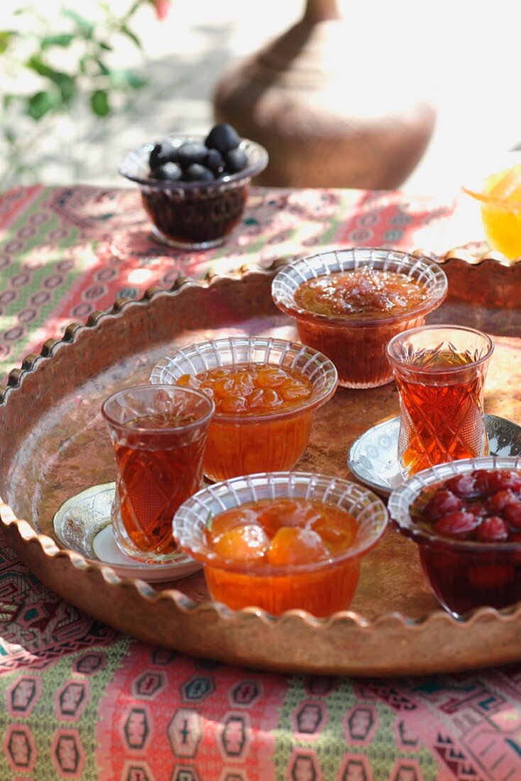 Gläser mit Tee & kandierte, eingelegte Früchte auf Tisch im Freien