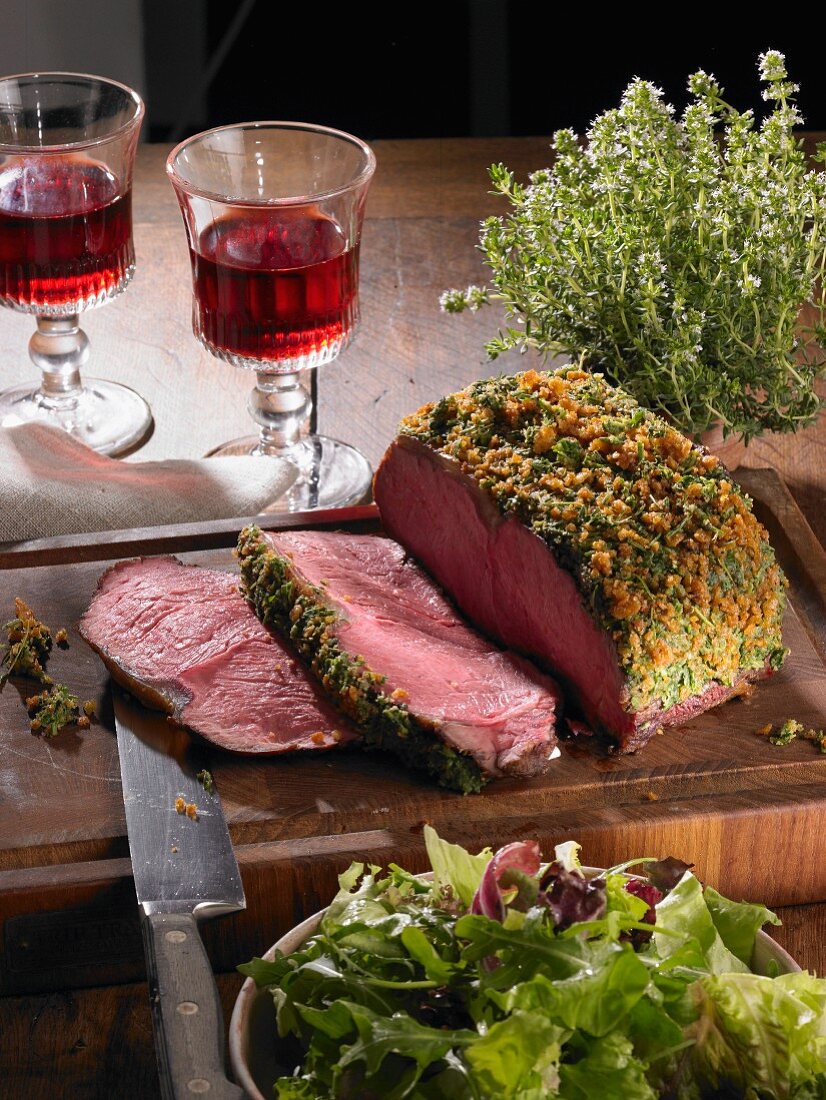 Sliced roast beef with a herb crust on a wooden board