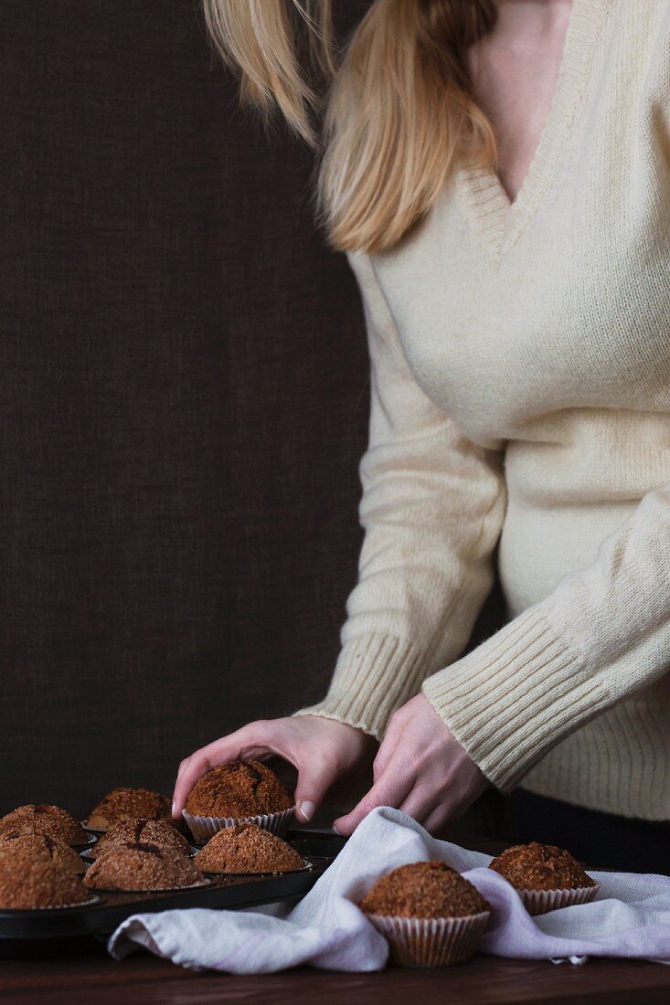 A woman removing cinnamon muffins from a muffin tin