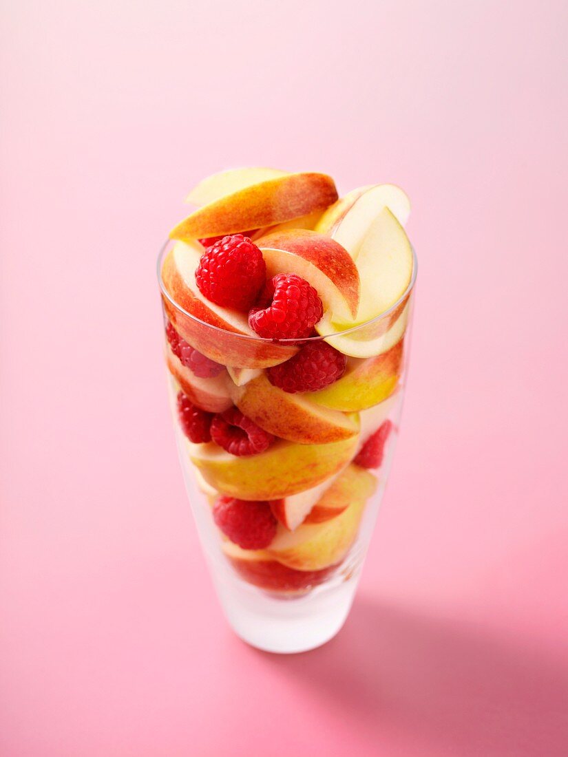 Apple wedges and raspberries in a glass on a pink surface