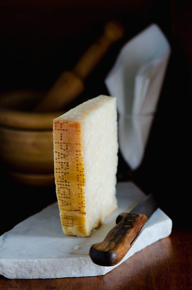 A slice of Parmesan cheese with a knife on a slab of marble