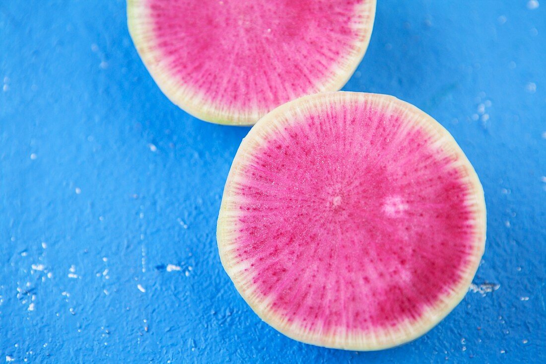 Pink radish slices on a blue surface (close-up)