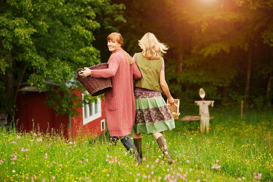 Two women walking arm in arm through a meadow with a wicker basket