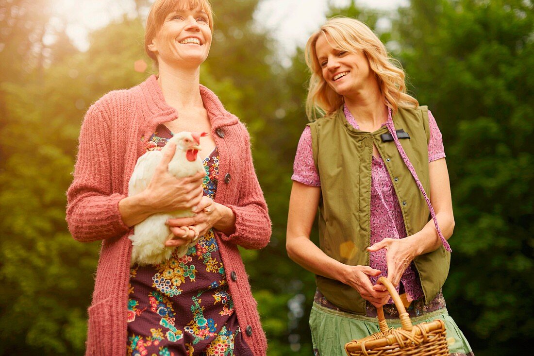 Two women with a chicken and a wicker basket in a meadow