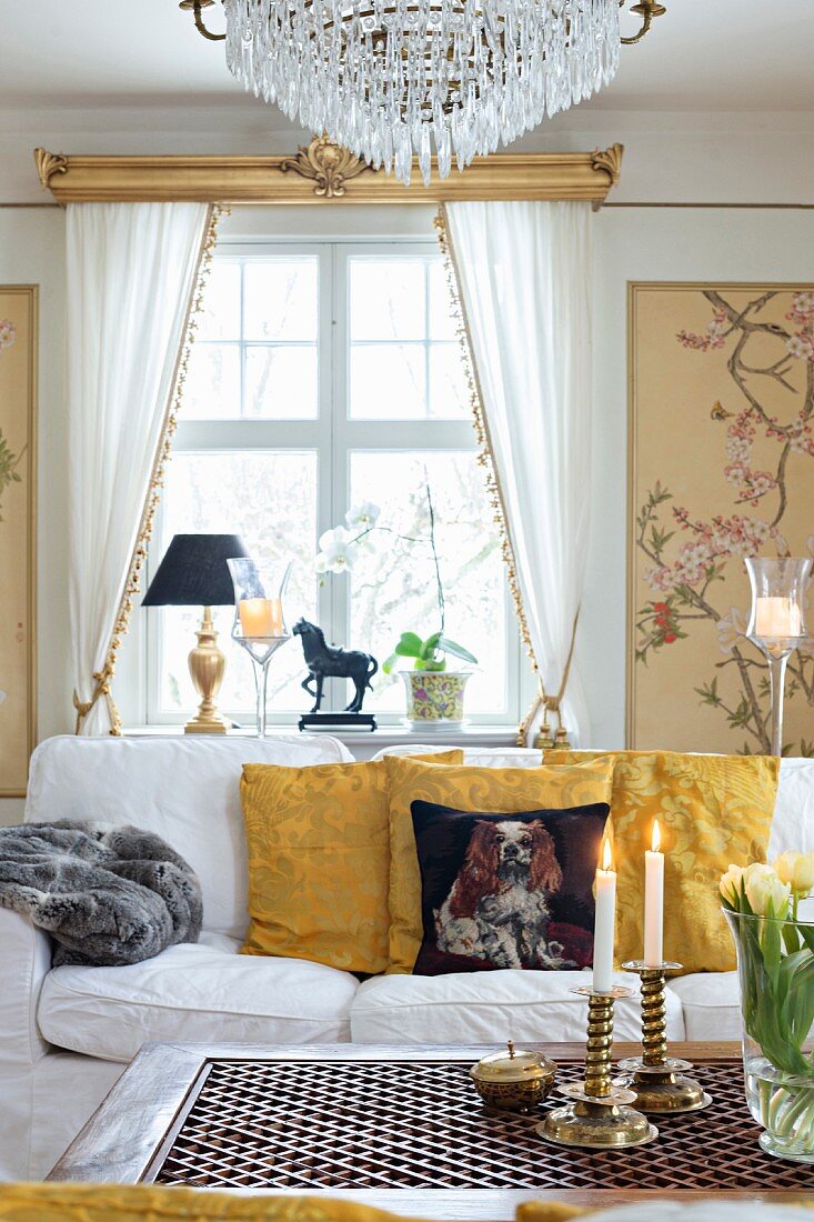 Coffee table in front of sofa with scatter cushions and window with white draped curtains