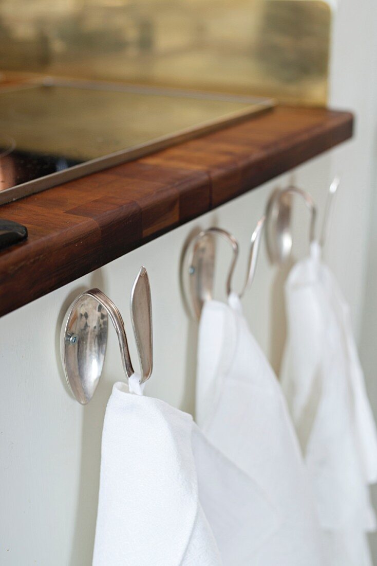 Tea towels hanging from dessert spoons bent into hooks