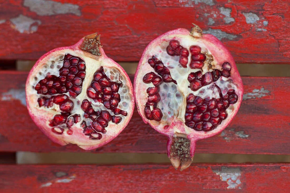 A halved pomegranate on a red wooden surface (seen from above)