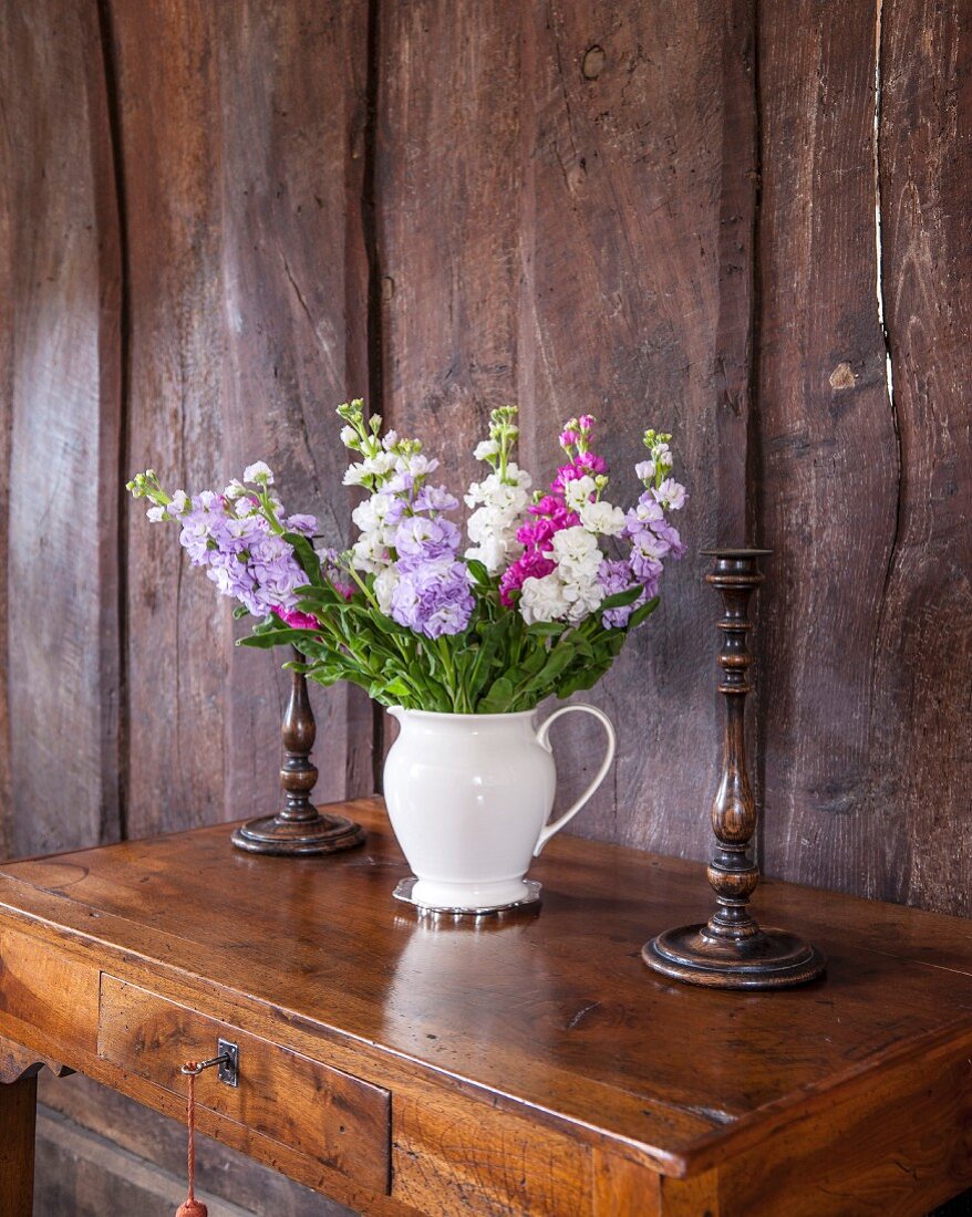 White jug of summer flowers on antique writing desk against rustic board wall