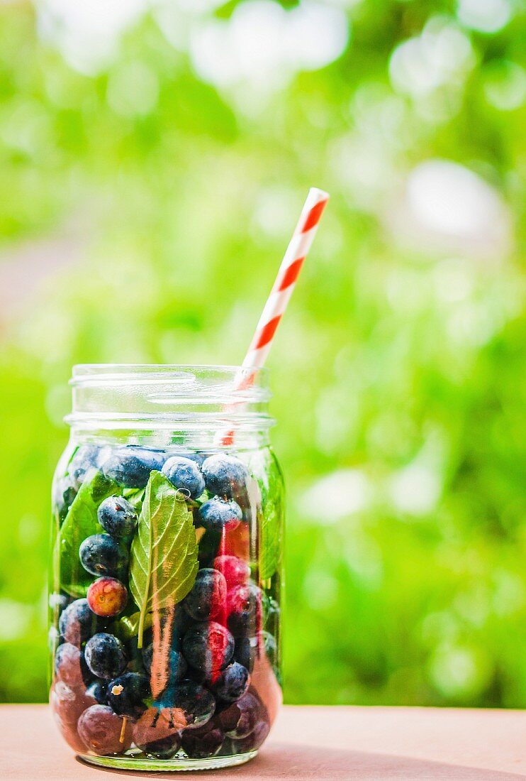 Iced tea with blueberries in a screw-top jar with a straw on a garden table