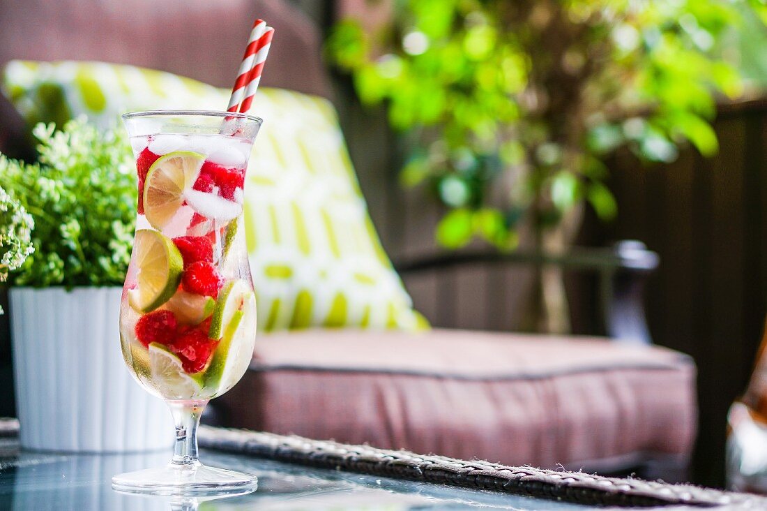 Eistee mit Früchten im Longdrinkglas mit Strohhalmen auf Gartentisch