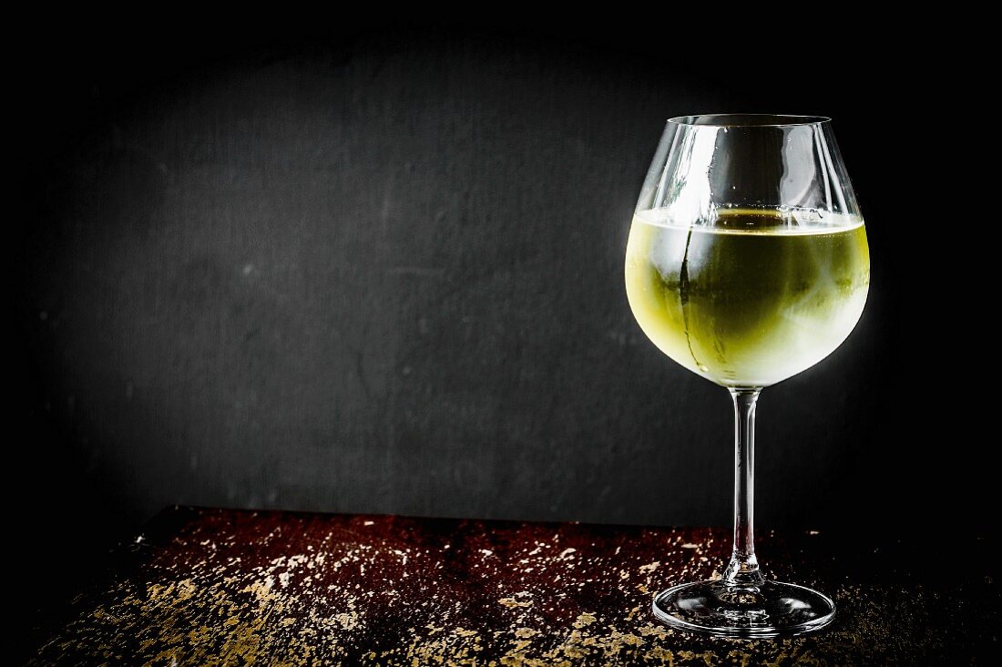 A glass of white wine against a black background