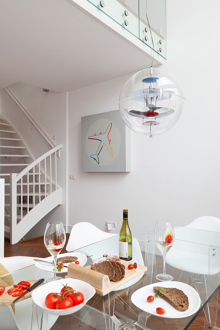 Set glass table below classic Verpan pendant lamp in open-plan interior with white-painted wooden staircase in background