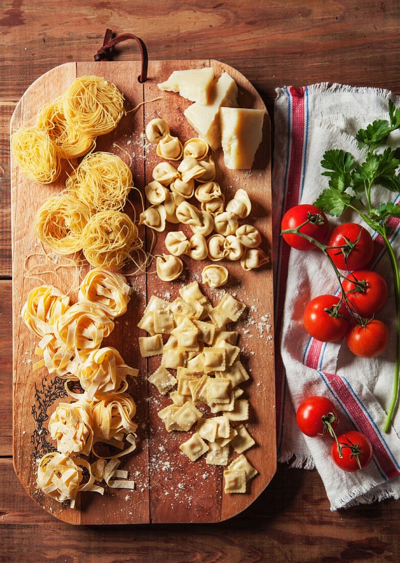 Various types of fresh pasta on a chopping board with Parmesan cheese, tomatoes and coriander