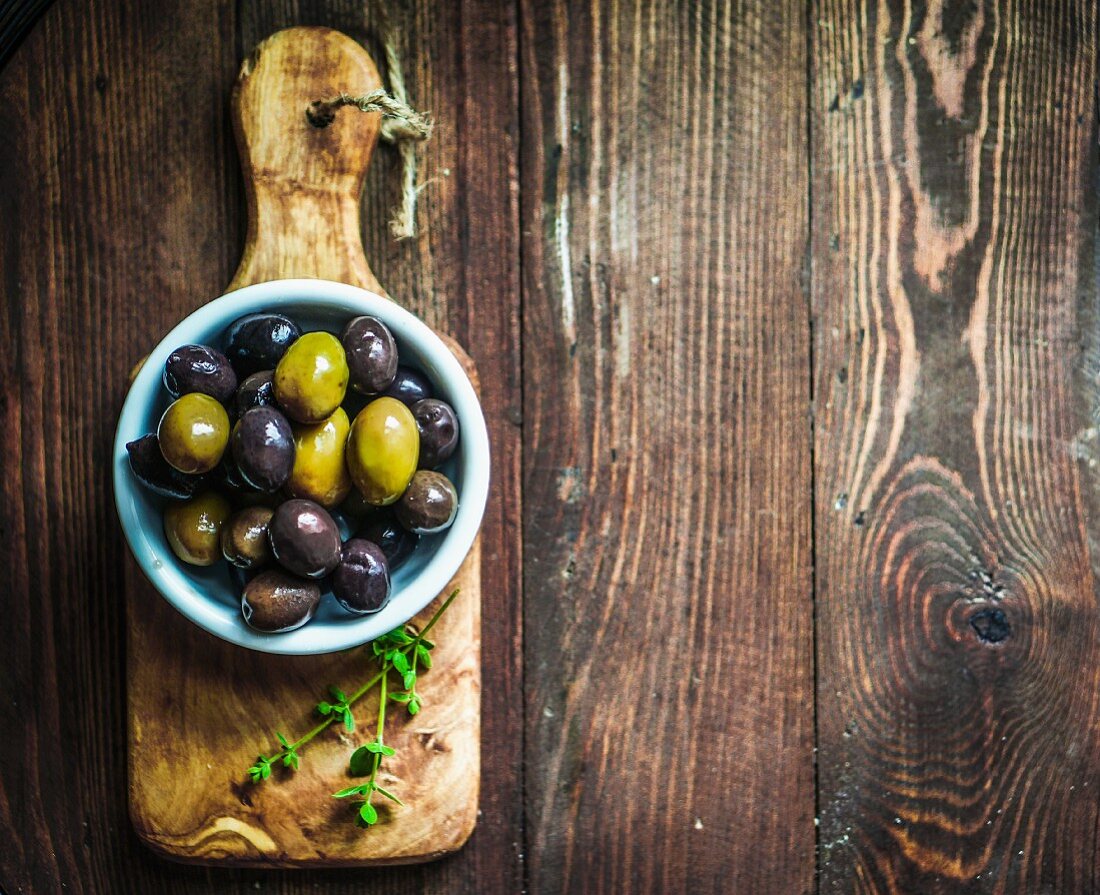 Green and black olives in a dish on a chopping board (seen from above)