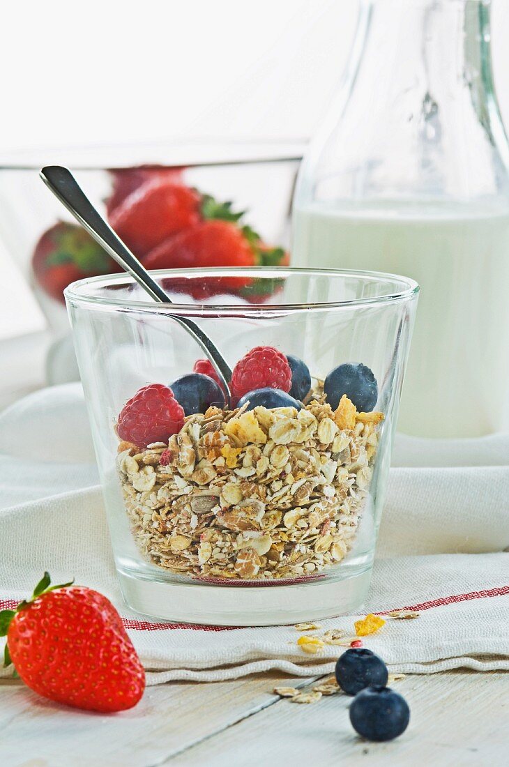 Gesundes Frühstück: Müsli mit frischen Früchten und Milch, Erdbeeren, Himbeeren, Heidelbeeren auf Holztisch