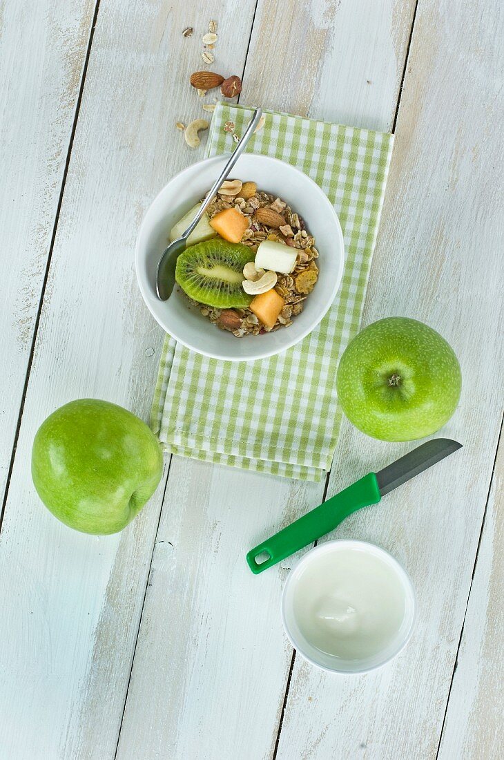 Gesundes Frühstück: Müsli mit frischen Früchten, Nüssen und Milch, Kiwi, Melone, Apfel auf Holztisch