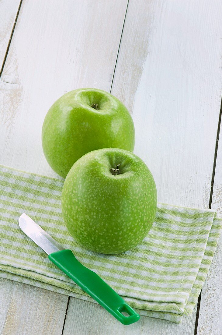 Two green apples on a napkin with a knife