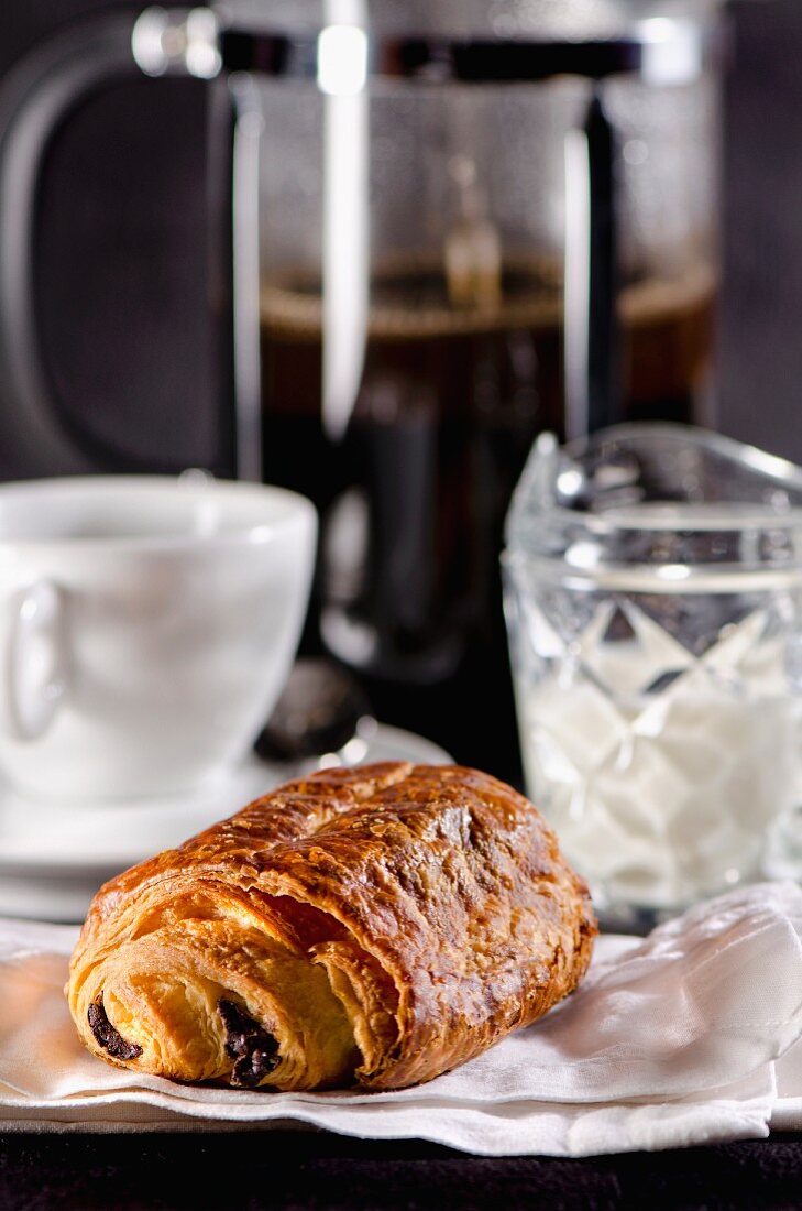 A pain au chocolat with a coffee cup and a coffee machine in the background (France)