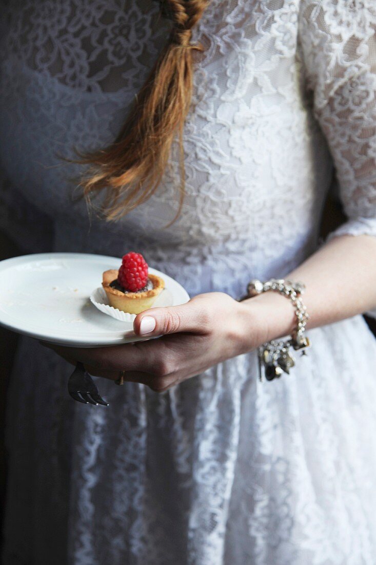 A bride holding a mini chocolate and raspberry tartlet on a plate