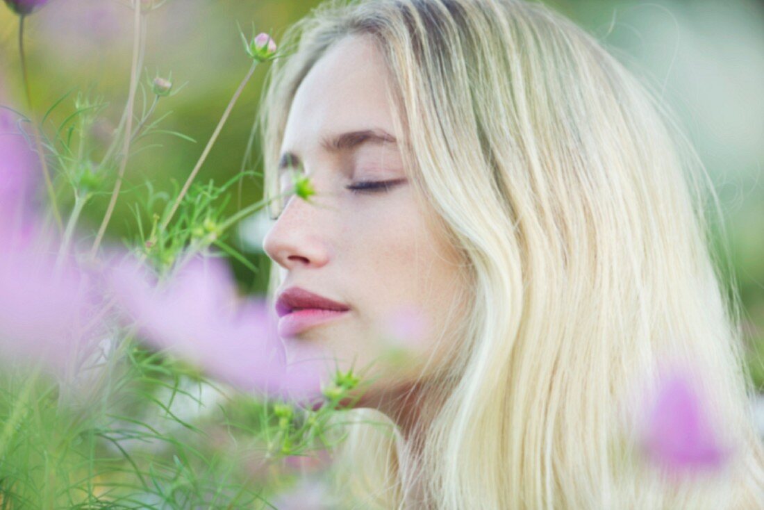 A portrait of a young woman in a field of flowers with her eyes closed