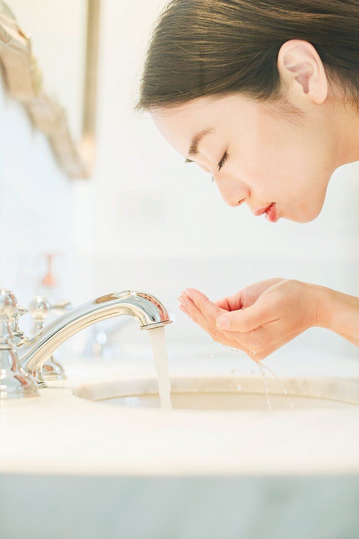 Asiatische Frau wäscht sich Gesicht am Waschbecken