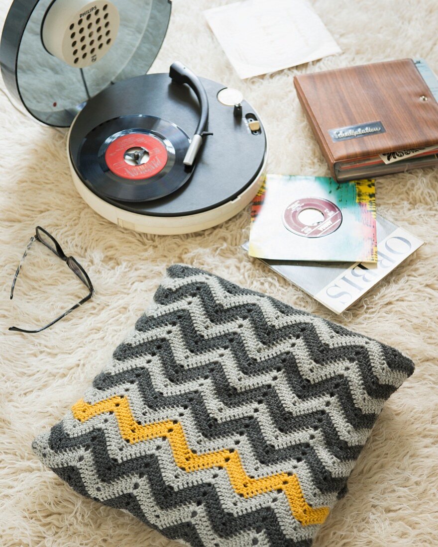 Crocheted cushion cover on flokati rug next to a record player