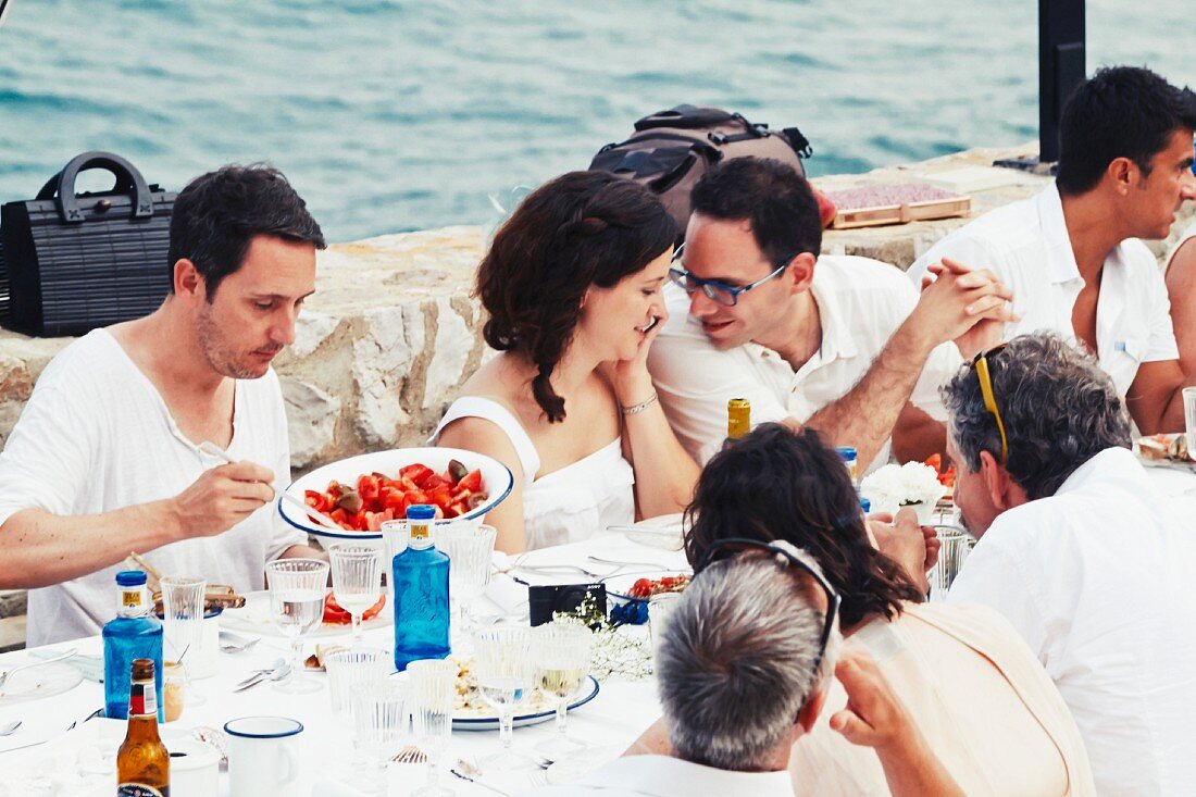 A bride and groom and guests eating by the sea