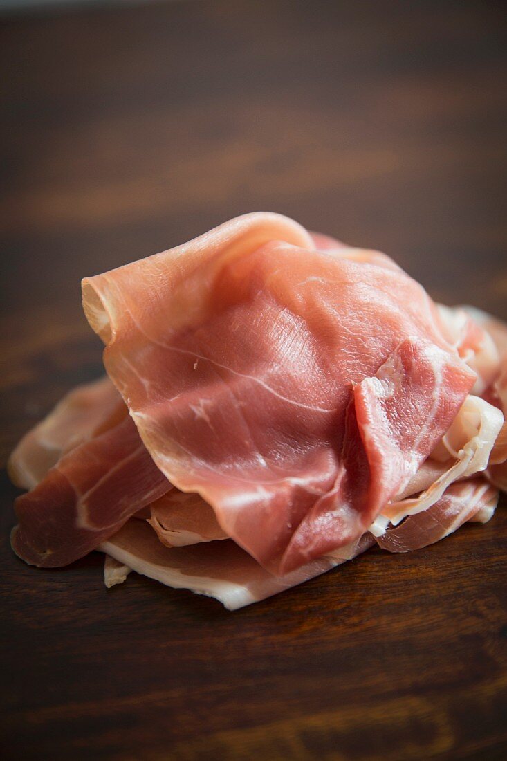 A pile of Parma ham slices on a wooden board