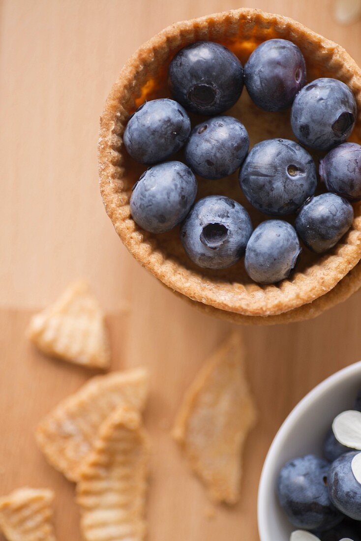 A shortcrust pastry dish with blueberries and a bowl of blueberries and hydrangea flowers (seen from above)