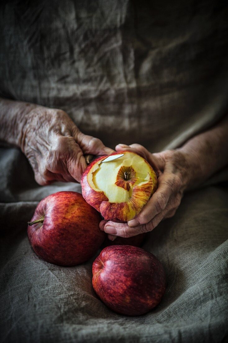 Alte Hände schälen rote Äpfel