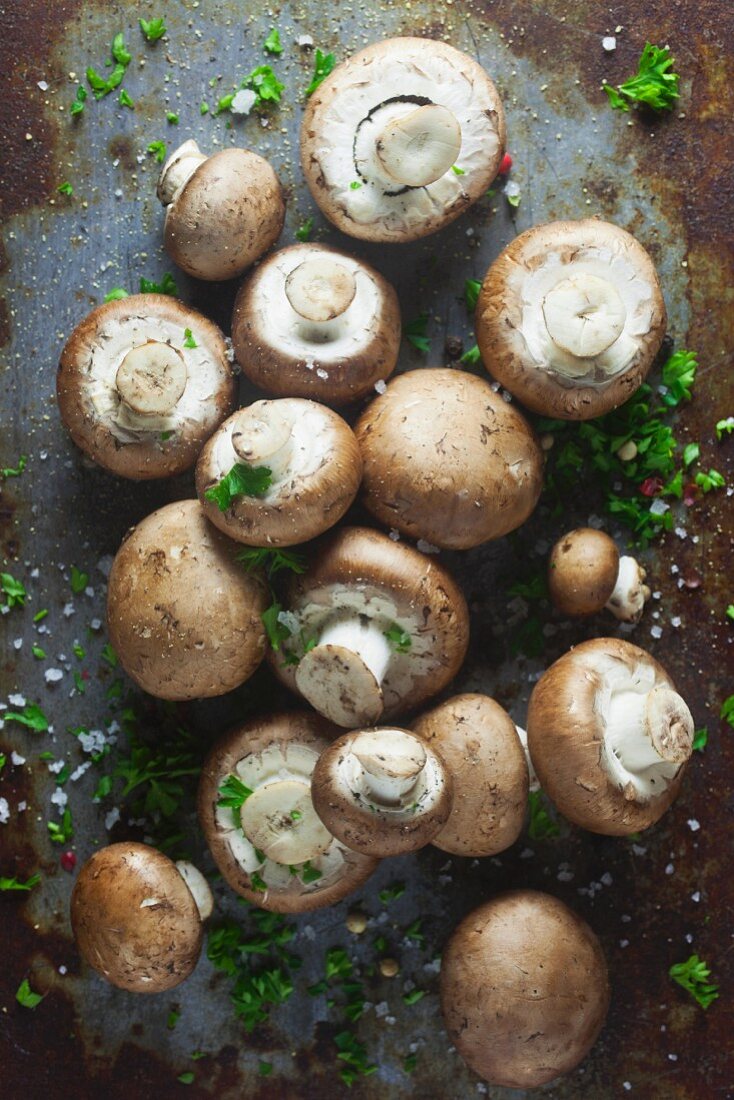 Brown mushrooms with parsley, pepper and salt on a metal surface