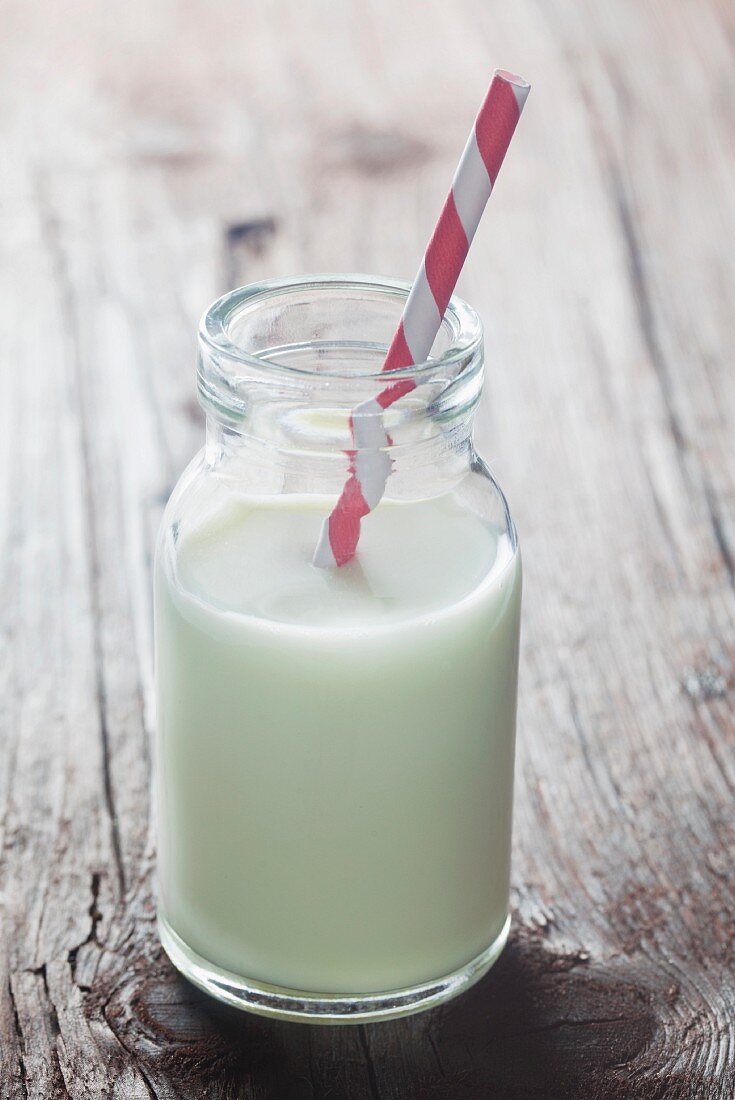 A bottle of milk with a straw on a wooden surface