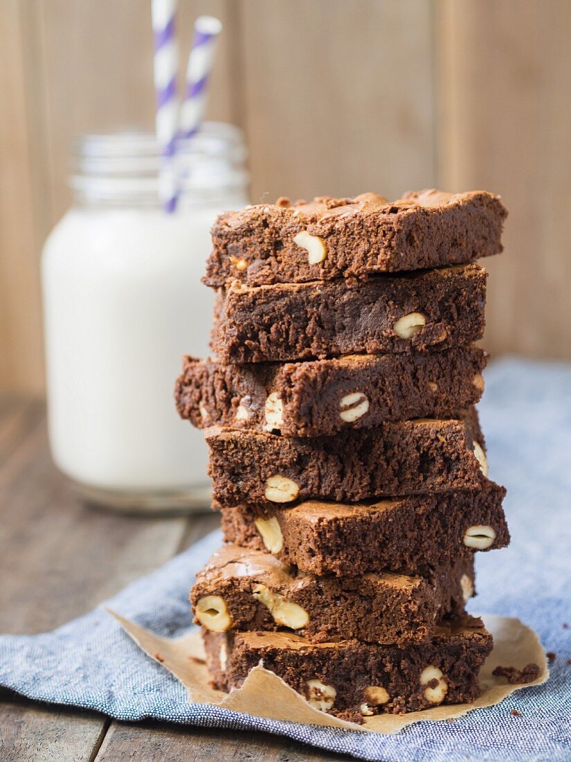 A stack of wholegrain organic brownies with cashew nuts and a glass of milk in the background